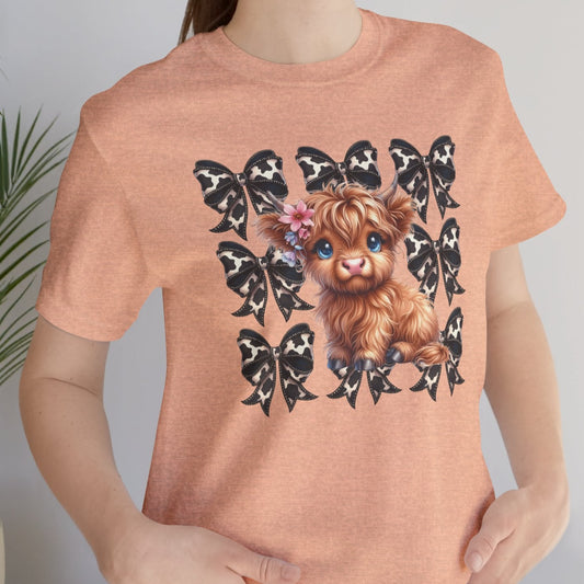 A person wearing a short-sleeved orange t-shirt with a graphic of a highland cow and surrounded by birds.