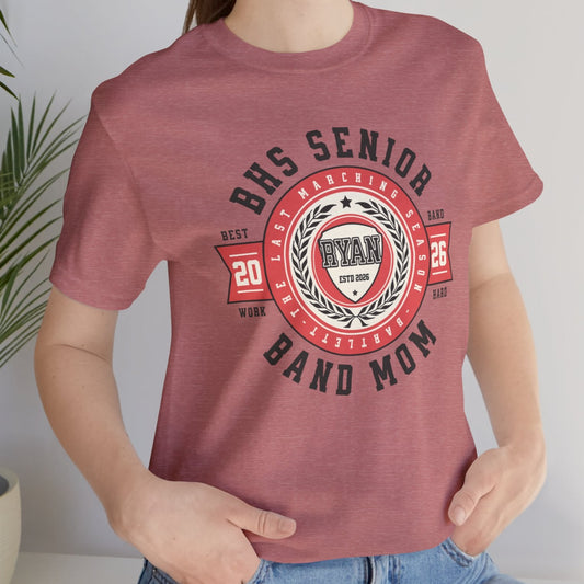 Person wearing a maroon t-shirt with 'BHS Senior Band Mom' design, standing indoors next to a plant.