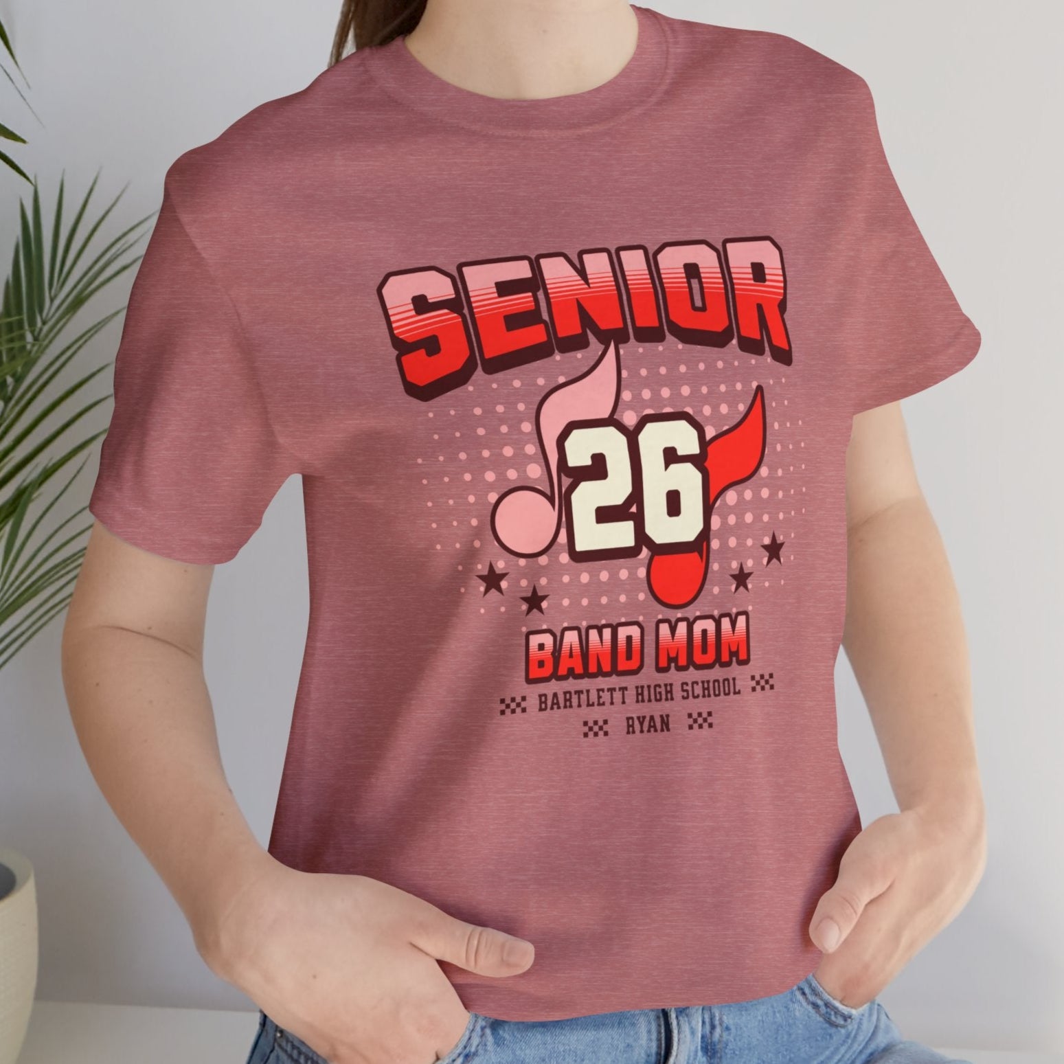 Person wearing a 'Senior 26 Band Mom' t-shirt with a plant in the background