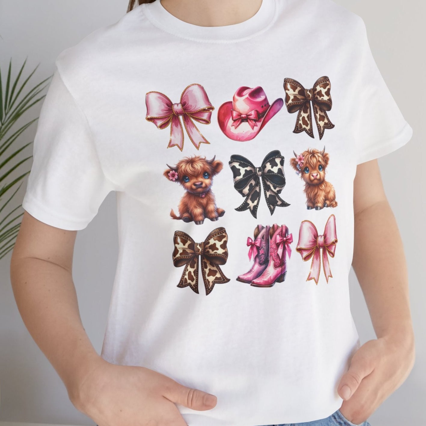 A person wearing a white short-sleeved t-shirt with graphic prints of dogs, bows, and shoes in pink and black colors.