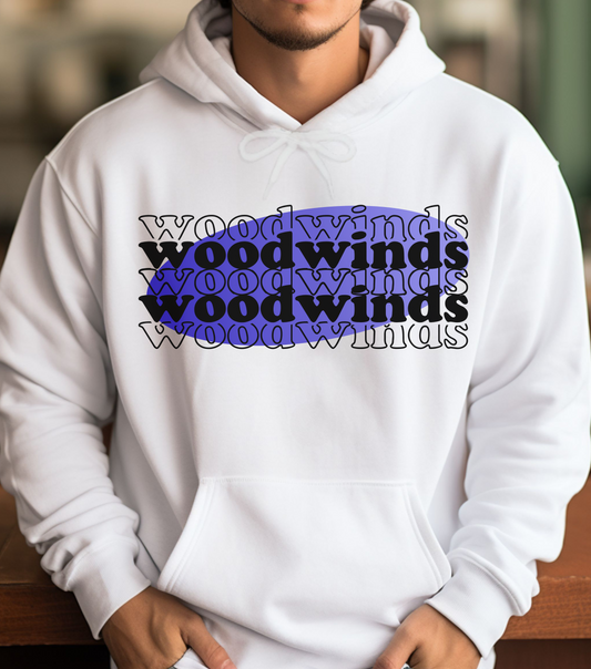 A person wearing a white hoodie with the text 'WOODWINDS' printed in purple on the front, sitting in a casual setting with a blurred background.